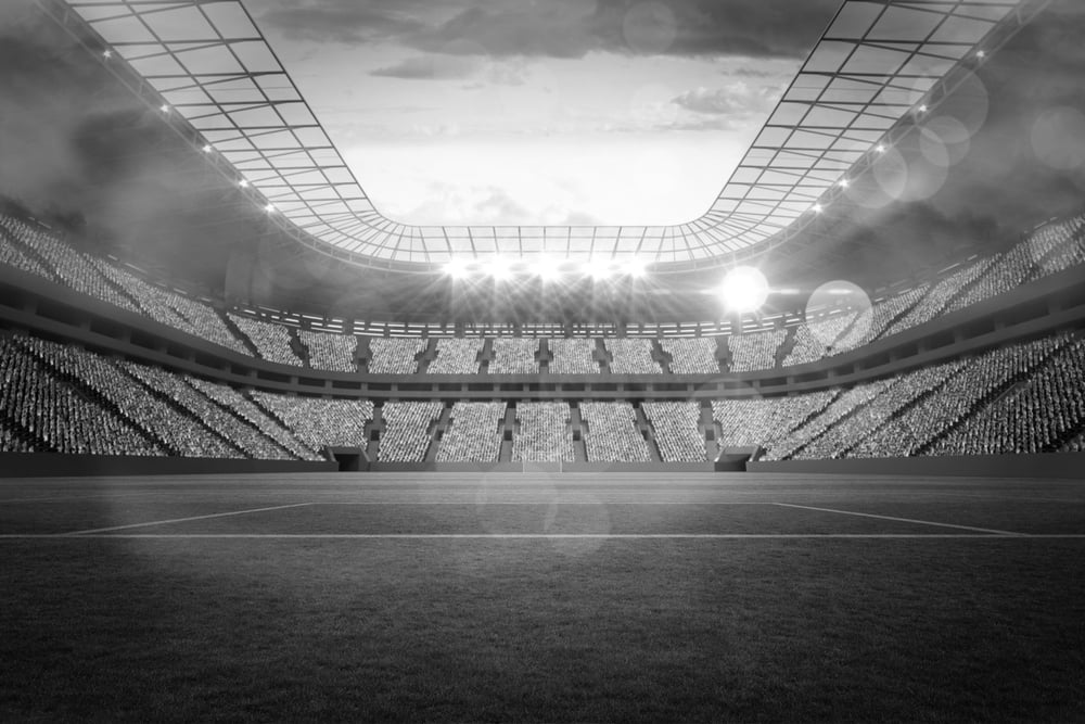 Large football stadium with lights under cloudy sky-bw
